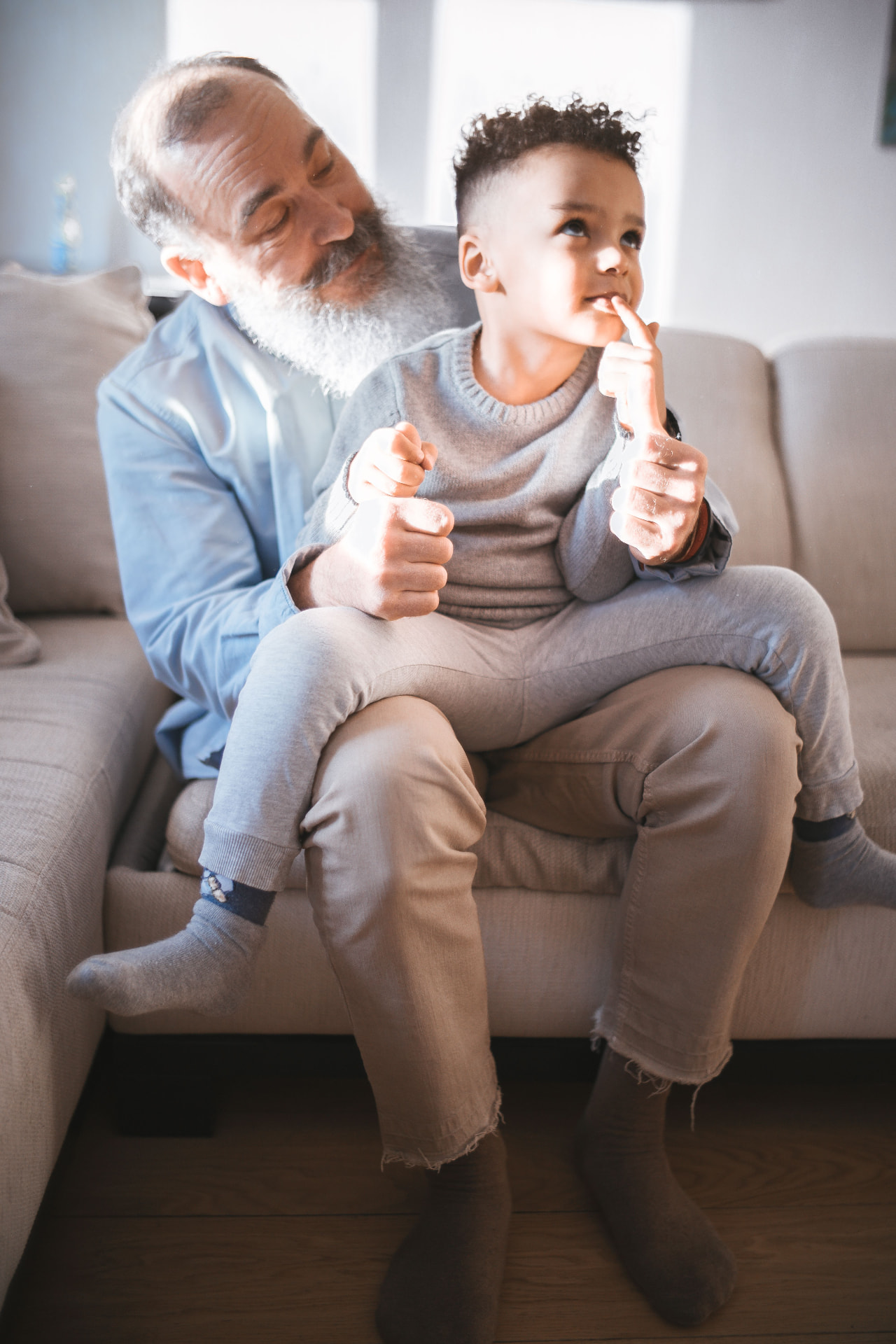 An older man and a young child sitting together on a sofa at home in daylight